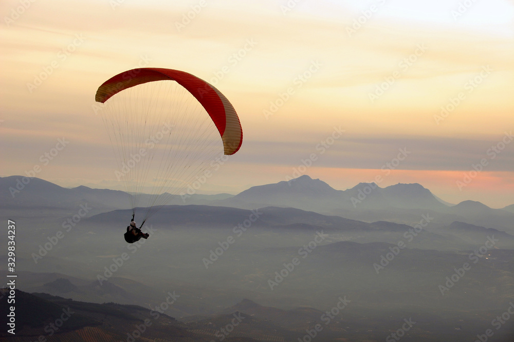 Paraglider flying at sunset in valley with mist and mountains in the background. Paraglider flying at sunset in valley with mist and mountains in the background.