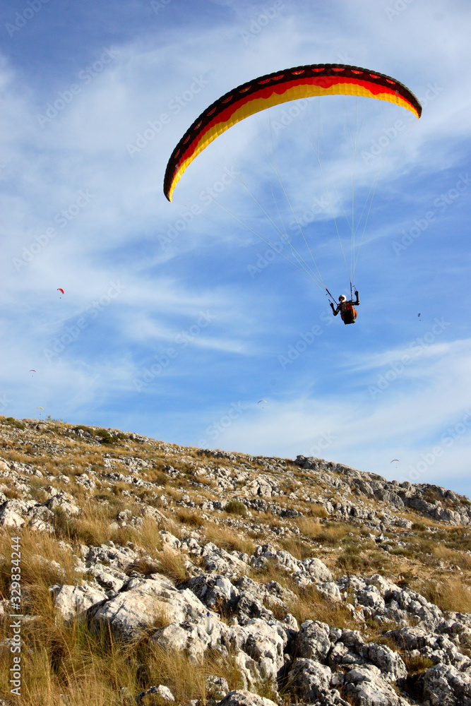 Paraglider flying low over hillside of stones and thickets and blue sky. Paraglider flying low over hillside of stones and thickets and blue sky.