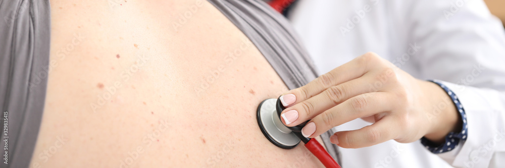 Close-up view of patients back. Young female doctor investigating respiration using red stethoscope. Physician checking lugs. Healthcare and medicine concept