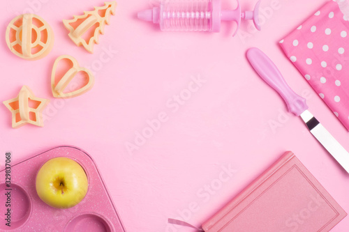 Cupcakes baking dish, a spatula, a recipe book, a towel on a pink concrete background. Monochrome. Copy space.