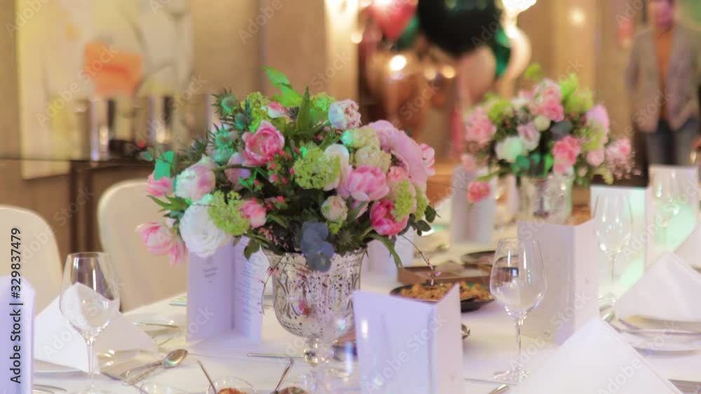 Beautiful served table at beginning of birthday party. Vase with flowers in focus. Guests arrive in blurry background Beautiful served table at beginning of birthday party. Vase with flowers in focus. Guests arrive in blurry background