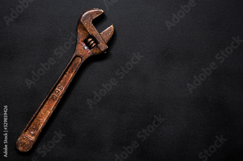 A rusty adjustable wrench for repairs lies on a black background