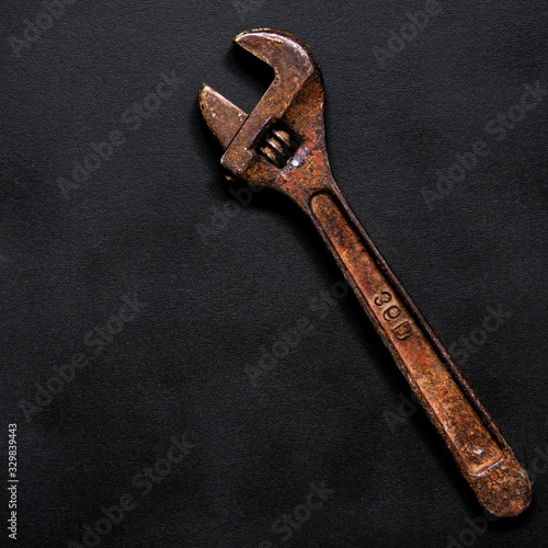 A rusty adjustable wrench for repairs lies on a black background