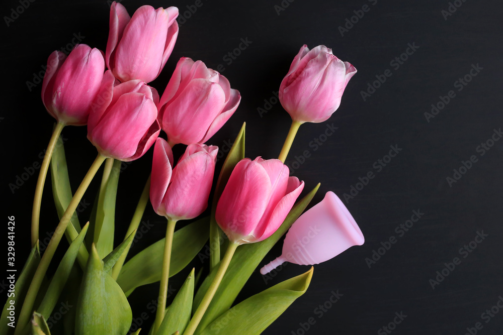 Obraz premium Menstrual cup and pink tulips on a black background. Menstruation, means of protection. Women's health, lifestyle.