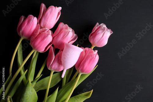 Menstrual cup and pink tulips on a black background. Menstruation, means of protection. Women's health, lifestyle. © Kristina