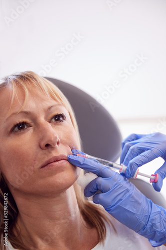 Mature Woman Sitting In Chair Being Give Anti Ageing Injection By Female Doctor