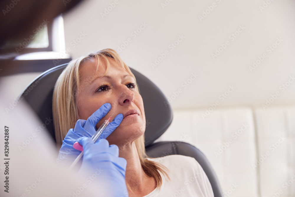 Mature Woman Sitting In Chair Being Give Anti Ageing Injection By Female Doctor Mature Woman Sitting In Chair Being Give Anti Ageing Injection By Female Doctor