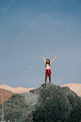 Mujer joven levantando sus brazos parada sobre una montaña