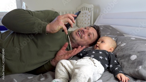 Happy father an a cute baby boy facetiming mommy on a cell phone on a bed photo