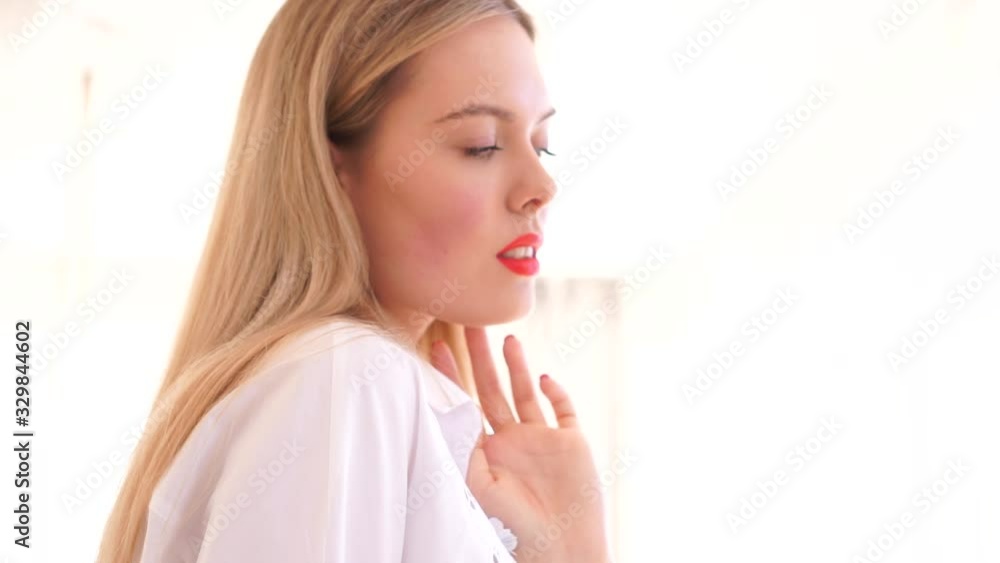 Portrait of a young white-haired girl by the window. Pretty young girl in a white shirt near the window. In the video, the girl poses against a large window. Light room. Portrait of a young white-haired girl by the window. Pretty young girl in a white shirt near the window. In the video, the girl poses against a large window. Light room.