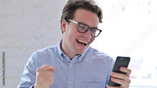 Portrait of Young Man Celebrating Success on Smartphone © stockbakers