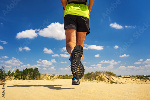 Athlete runs along the sandy desert. Desert trail running. A man in shorts and a T-shirt is running through the sandy wilderness photo