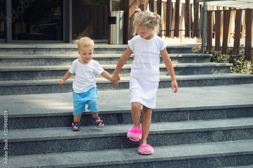 Two cute adorable caucasian blond little siblings walking down stiars residential building. Reliable elder sister support, learnd and help younger toddler brother. Family love, care support photo