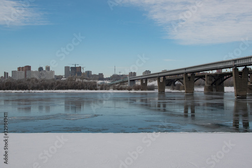 Urban landscape in spring, melting snow on the river, bridge over the river, construction in the city © seregg