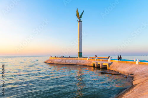 The pier of Campeche city illuminated at sunset with the angel of miscegenation (indigenous and Spanish) and its waterfront promenade by the Gulf of Mexico, Campeche state, Mexico. photo