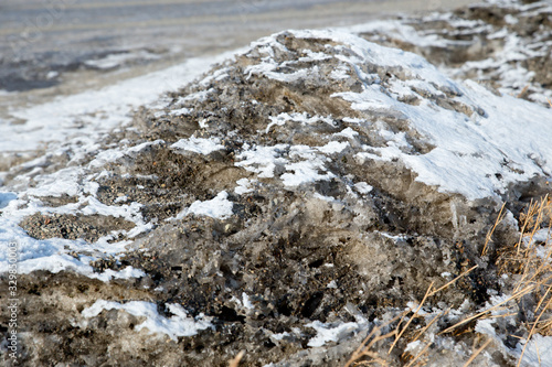 Melted mud on the side of the road. Dirty snow spring background. Old and dirty snow texture. Natural background. Snow mixed with coal soot, poor ecology.