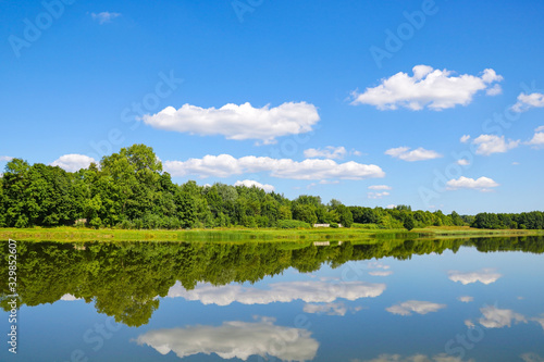 Reflection of white clouds and forest in a river or lake on a sunny day, nature.