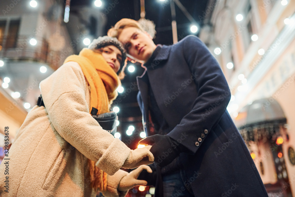 Closeness of the people. Happy young couple in warm clothes is on christmas decorated street together Closeness of the people. Happy young couple in warm clothes is on christmas decorated street together