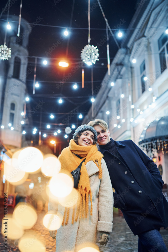 Cute couple in warm clothes is on christmas decorated street smiling and have fun Cute couple in warm clothes is on christmas decorated street smiling and have fun