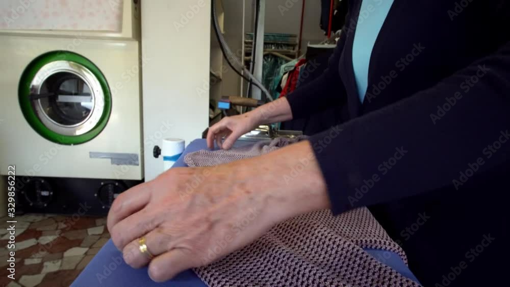 Older female ironing a folded shirt garment at a laundromat store, locked tripod shot Older female ironing a folded shirt garment at a laundromat store, locked tripod shot