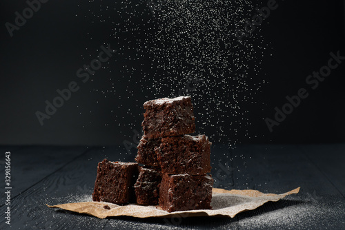 Stack of a brownie pieces on a grey table with dark background with sugar powder snow. photo