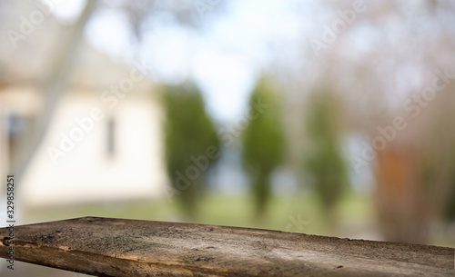 An empty wooden tabletop on a window pane and abstract green blur from the garden with a view of the yard, can be used to display or assemble your products (or products).