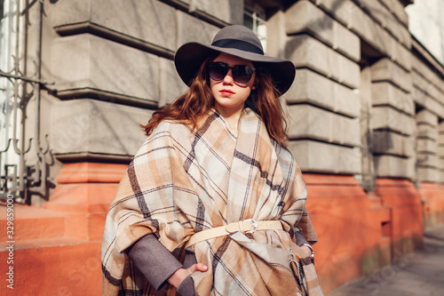 Outdoor portrait of stylish young woman wearing hat glasses poncho. Spring fashion female retro accessories outfit photo