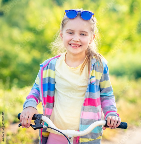 Adorable smiling girl riding small modern bike with colorful jacket outdoors photo