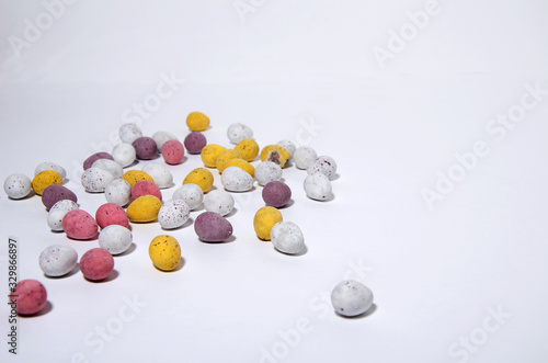 Small sweet candies in the shape of Easter eggs lie randomly on a white background. Different colors - white, yellow, purple, horizontal view