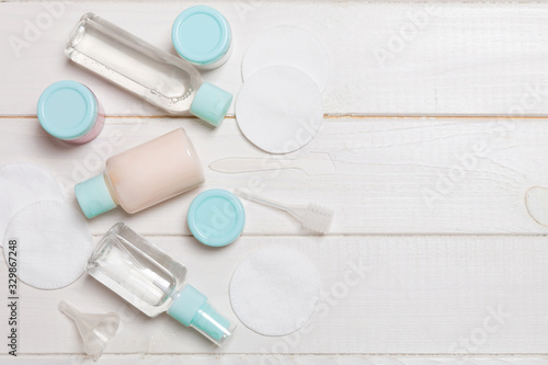 Group of small bottles for travelling on wooden background. Copy space for your ideas. Flat lay composition of cosmetic products. Top view of cream containers with cotton pads