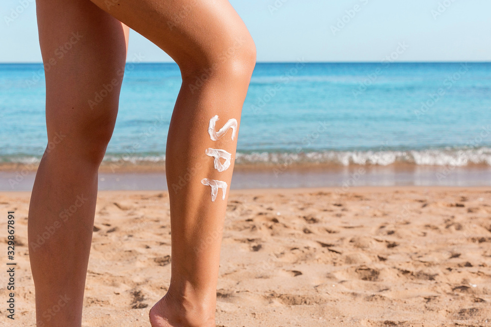 Female legs with spf word made of sun cream at the beach. Sun protection factor concept Female legs with spf word made of sun cream at the beach. Sun protection factor concept