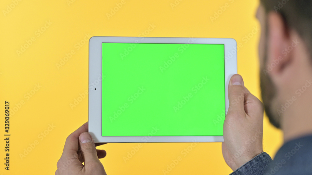 Rear View of Young Designer Scroll on Tablet with Chroma Screen, Yellow Background Rear View of Young Designer Scroll on Tablet with Chroma Screen, Yellow Background