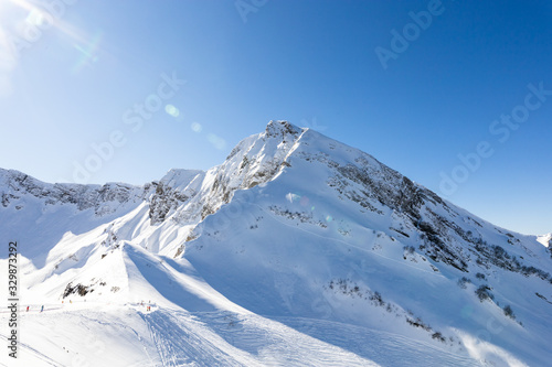 Beautiful snowy mountain panorama, clear blue ski background, few unrecognizable riders and ski lines on it. Horizontal picture with back light. Actual extreme hobby and lifestyle.