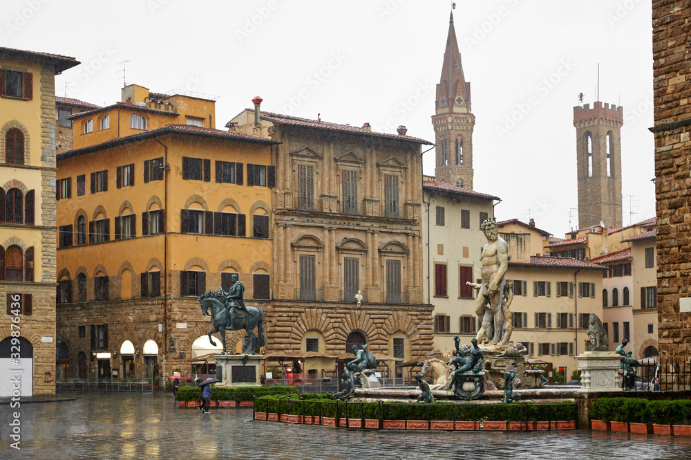 Florence Italy. Piazza della Signoria with view at Neptune Fountain with bronze statues in rainy weather day and antique houses and tower.