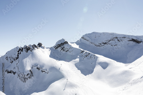 Wonderful panorama of high snowy rocky mountains with nobody on it, but ready pillars for cable car and few ski lines under them. Bright sunny day, blue sky. Horizontal image. Actual lifestyle.