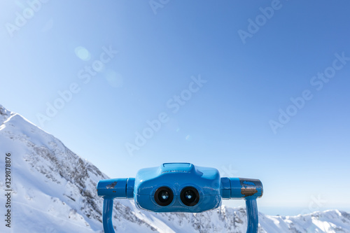 Touristic binoculars, device for sightseeing, stationary viewing binoculars, viewing binoculars with  coin operator, with view on beautiful snowy mountains on background, shoot taken with back light 