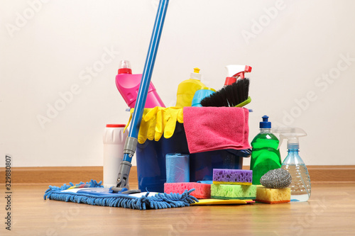 Various bottles with cleaning products and detergents, washcloths in a blue bucket and a mop in the room on the floor
