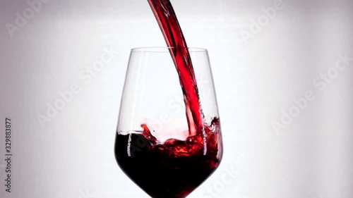 Slow motion of pouring red wine from bottle into goblet. Close-up of red wine forms beautiful wave in glass. Wine pouring in glass at white background.