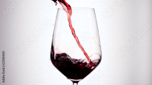 Slow motion of pouring red wine from bottle into goblet. Close-up of red wine forms beautiful wave in glass. Wine pouring in glass at white background.