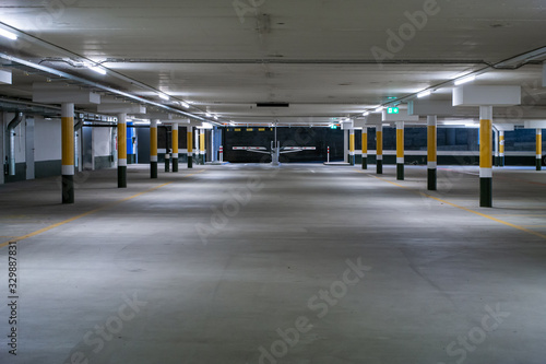Inside underground large empty parking lot with barrier entrance at night illuminated by neon light