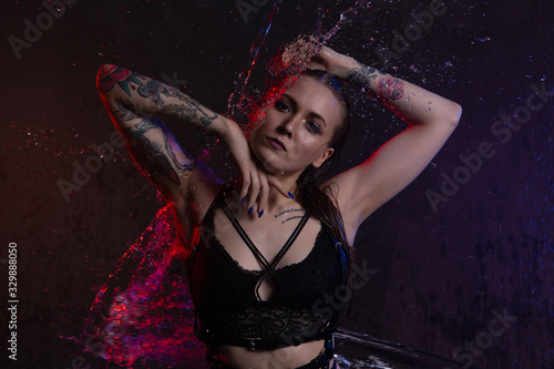 Fotografie A blonde girl in a swimsuit under the water jets with beautiful splashes in a da