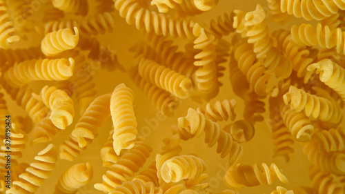 Freeze motion of flying uncooked italian pasta fusilli on golden background.