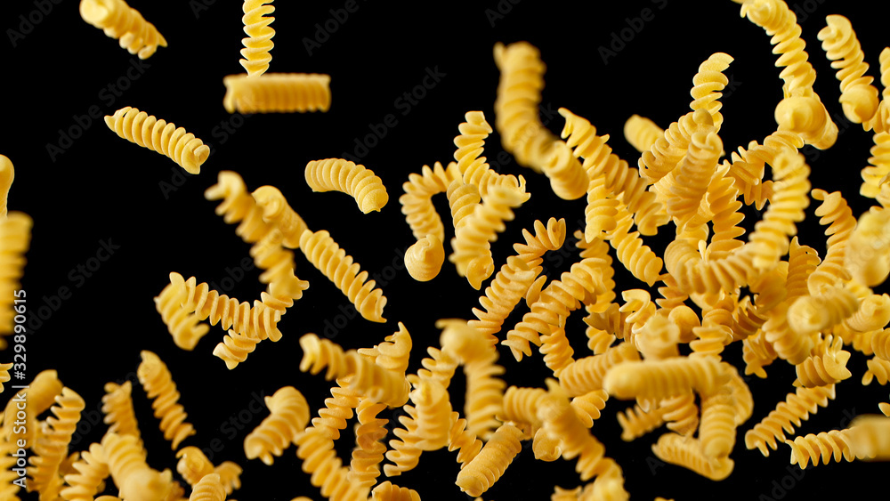 Freeze motion of flying uncooked italian pasta fusilli on black background.