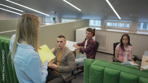 Angry female manager with binder walking down office corridor, entering cubicle and reproaching employee working at desk. Manager firing worker and asking him to leave office