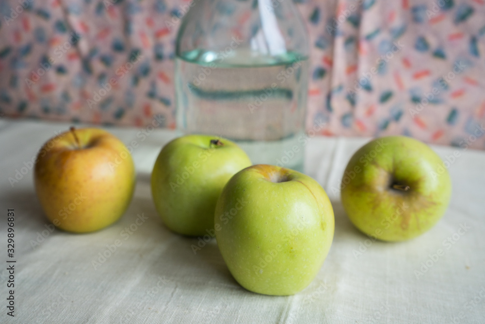 Still life with green apples and .water bottle on the table. Apples lie on a background of drapery Still life with green apples and .water bottle on the table. Apples lie on a background of drapery