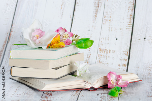 Stack of textbooks on a light wooden background are decorated with beautiful flowers photo