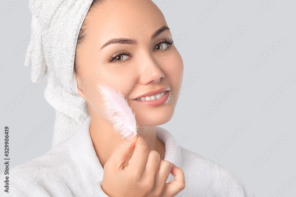 Portrait of a beautiful happy woman with clean skin on a gray background. She holds a pink feather near her face. Cosmetology and skin care. Portrait of a beautiful happy woman with clean skin on a gray background. She holds a pink feather near her face. Cosmetology and skin care.