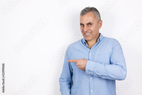 mature handsome man with grey hair wearing blue shirt standing on isolated white background points with his finger, body language concept © studioprodakshn