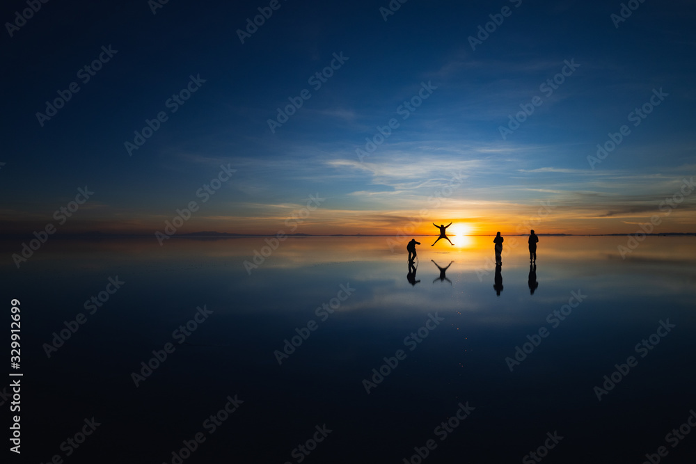 Uyuni Salt Flat, Bolivia, South America - Silhouettes of Tourists taking photos at sunrise having fun with the reflection from a thin layer of water during the rainy season