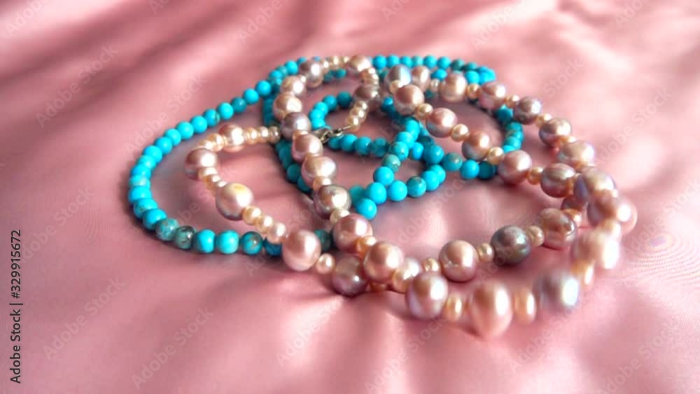 A pearl necklace and rings fall on silk. Slow motion.